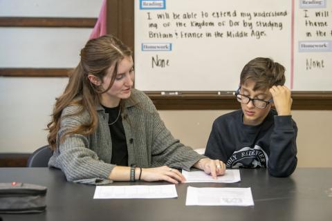 ACE 30 Teacher Grace Rakestraw (left) chatting with student (right) and pointing to worksheet on table in front of them. 